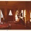 A photograph showing another section of the vintage hotel room featuring another poker table, a  fireplace, tv set and cusioned chairs.