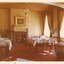 A photograph of a vintage dining room with elaborately laid out tables, a fireplace and a gilded painting hanging above it.