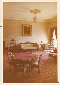 A photograph of a vintage room with poker tables, a lounge and a gilded painting hanging above it.