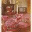 A vintage sitting room with red upholstered furniture, patterned carpet, a fireplace with a clock on the mantel and an old television set.