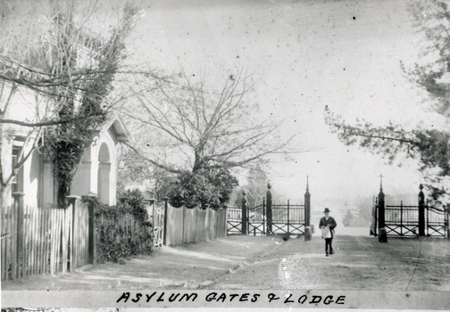 A black and white photograph featuring a man entering the front gates of the Mental Hospital.