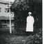 A black and white photograph featuring a nurse in uniform at the Mental Hospital in Beechworth, with a fern house behind her.