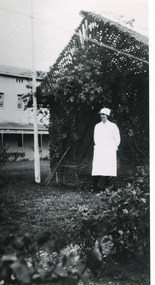 A black and white photograph featuring a nurse in uniform at the Mental Hospital in Beechworth, with a fern house behind her.