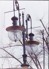 Black and white photo of old gas street lamp with leafless tree behind it.