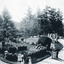 An outdoor photograph showing many groups of people, mostly in two and three, dressed in period clothing in a well manicured garden during the day. 