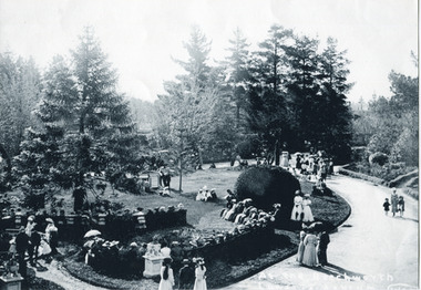 An outdoor photograph showing many groups of people, mostly in two and three, dressed in period clothing in a well manicured garden during the day. 