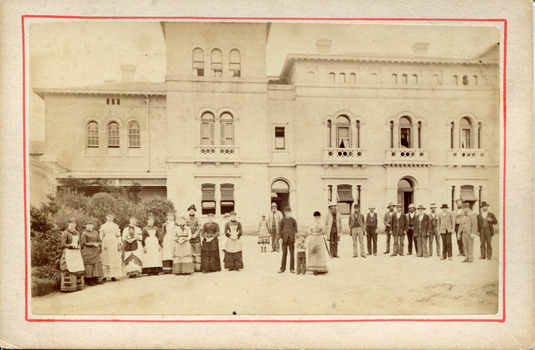 Out front of the Beechworth mental asylum administration building is twenty-eight staff members divided by gender with females on the left and males on the right. There is a child in the center 