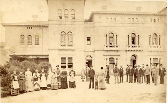 Out front of the Beechworth lunatic mental administration building is twenty-eight staff members divided by gender with females on the left and males on the right. There is a child in the center 