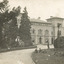 A pathway featuring manicured gardens on either side leading to the Beechworth Mental  Asylum administration building. There are four males, three are sitting on the grass while one stands on one leg just behind them.