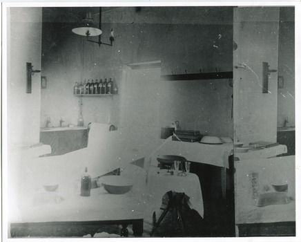 Grainy black and white photograph showing interior of surgery and consulting room in the Mental Hospital. Tables with medical instruments, bowls and jars are visible. Lefthand section of the photograph has been reproduced on the righthand side to show details which are lost due to overexposure. 