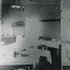 Grainy black and white photograph showing interior of surgery and consulting room in the Mental Hospital. Tables with medical instruments, bowls and jars are visible. Lefthand section of the photograph has been reproduced on the righthand side to show details which are lost due to overexposure. 