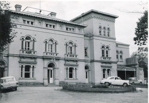 Rectangular black and white photograph of Beechworth Mental Hospital  (Mayday Hills) facing towards the right hand side of the administrative building with three cars parked in driveway turning circle in the foreground.