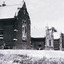 Black and white photograph of front view of Ovens Benevolent Home with one person sitting on a bench seat against the nearest part of the building and another person walking on the grass.