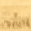 Group of workmen in hats standing in front of an old building, the sign of which reads "The Ovens and Murray Advertiser." 