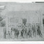 Group of workmen in hats standing in front of an old building, the sign of which reads "The Ovens and Murray Advertiser."