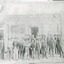 Group of workmen in hats standing in front of an old building, the sign of which reads "The Ovens and Murray Advertiser."