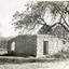 Ruins of a small stone building with a woman standing next to a tree looking at the building 