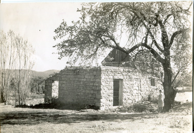 Ruins of a small stone building with a woman standing next to a tree looking at the building 