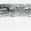 Uncropped black and white photograph (top half of paper) of a row of business buildings on a rocky, sloping hillside, with a view across to residences and open land. Businesses from left to right (up the slope): J.E. Bishop, Coach Builders; Straughair Duncan, Engineers, Blacksmiths & Farriers; Straughair Duncan, Beechworth Foundry;  Wholesale & Retail Est. 1855 (?), Family Store Mackenzie; T. Pratten, Grocer - ?? & ?? Dealer, 