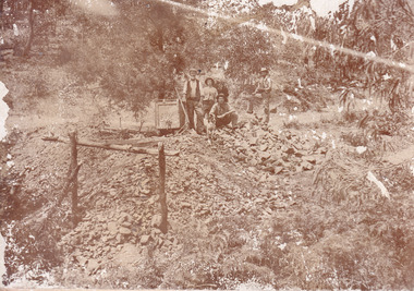 Four men and a dog standing at the entrance to 'Williams Good Luck Mine' (signposted on a wheeled cart on a track) in 1899. One man holds a second smaller dog. A large opening to a mine can be seen behind the men. Uneven rocks spill out of the mine entrance, with a timber frame in the foreground. A bush setting is around the mine. Image taken at the 800 ft Mopoke Gully-Stanley Tunnel. 