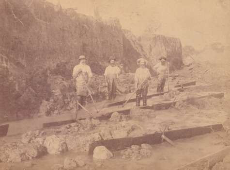 Four miners standing in mining sluice  at Three Mile Goldfields