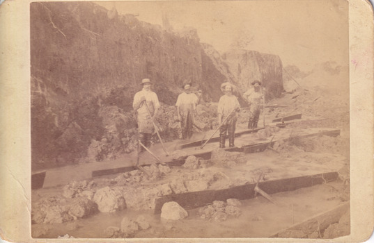 Four miners standing in mining sluice  at Three Mile Goldfields