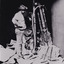 a man in a cowboy style hat (often worn in this era) standing next to mining machinery that is half a head taller than him