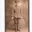 Mounted sepia photograph with black border of William Edward Peach,  a WWI soldier in uniform holding a crop across his thighs.