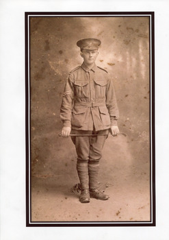 Mounted sepia photograph with black border of William Edward Peach,  a WWI soldier in uniform holding a crop across his thighs.