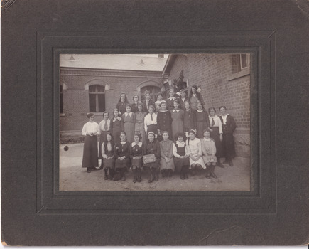 Framed photograph depicting a group of school girls and teachers posing outside a brick school building