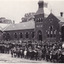 Black and white postcard of the Beechworth State School building. A large number of students and teachers standing in front of the building. 