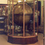 Large wooden world globe encased in a glass and wood display case, a person stands in the background behind the display case.