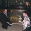 A crouching man and women surround a glass case containing a Thylacine, another women is standing next to the case. They are all smiling at the camera and behind them are hundreds of taxidermy specimens lining the wall, also in glass cases.