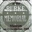 A black and white invitation to the Burke Museum Christmas party of 2005. In the background of the invitation is a stained glass window that says "Burke Memorial" with stars, floral designs and patterns.
