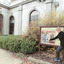 Woman dressed in warm clothes standing in front of an information sign pointing to a picture on the sign. In the background is the Burke Museum building.