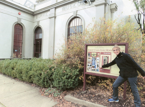 Woman dressed in warm clothes standing in front of an information sign pointing to a picture on the sign. In the background is the Burke Museum building.