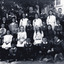A school class photograph showing 31 students and a teacher in uniform. They are standing in front of a building. 