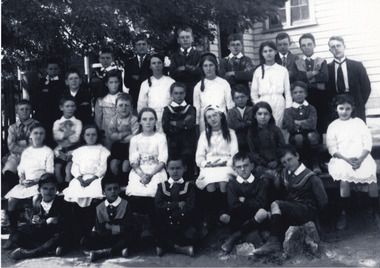 A school class photograph showing 31 students and a teacher in uniform. They are standing in front of a building. 