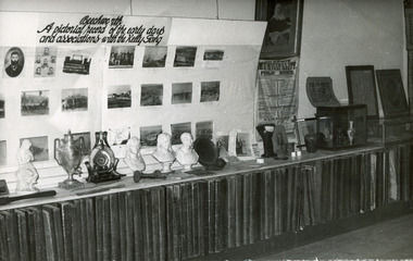 Black and white photograph of museum collection featuring busts, a photo display and other objects