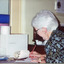 Colour photograph of woman sitting at desk, writing with a pencil.