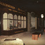 Colour  photograph featuring the shop frontage of Beechworth Bazaar with high arched windows and antique ware on display. Dimly lit streetscape lined with 19th-century lamp posts and benches, and a boulder with a plaque in the foreground. Source: Burke Museum Collection.