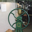 Colour photograph of grain mill as part of the Harvest Exhibition at Burke Museum in 1999. It features a grain mill, made by  B.M. Purshouse in Wolverhampton, England, with green wheels and base, and a gold container in which grain is poured. 