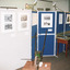 Colour photograph depicting a section of "The Harvest" exhibition with display cabinet containing objects and display boards containing photos and information.  In the foreground is believed to be an old seed distributor.