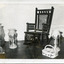 Black and white photograph of a rocking chair, a kerosene lamp, a bottle holder, and two epergnes.
