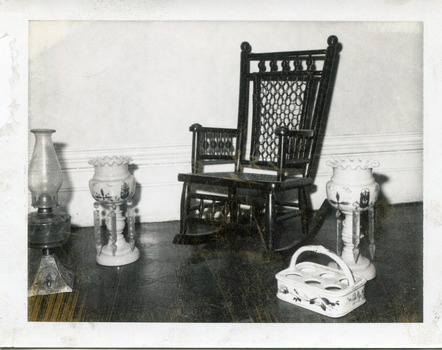 Black and white photograph of a rocking chair, a kerosene lamp, a bottle holder, and two epergnes.