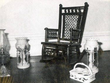 Black and white photograph of a rocking chair, a kerosene lamp, a bottle holder, and two epergnes.