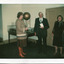 A colour photograph with a white boarder of two women and a man in front of an exhibition display table.