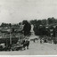 Black and white view of Camp Street and bridge over Spring Creek. Several people are on the bridge, and a horse and cart can be seen in the foreground.