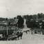 Black and white view of Camp Street and bridge over Spring Creek. Several people are on the bridge, and a horse and cart can be seen in the foreground.