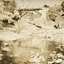 Sepia toned photograph of a creek with a bridge in the background, and a shallow creek in the foreground. A car can be seen crossing the bridge. 